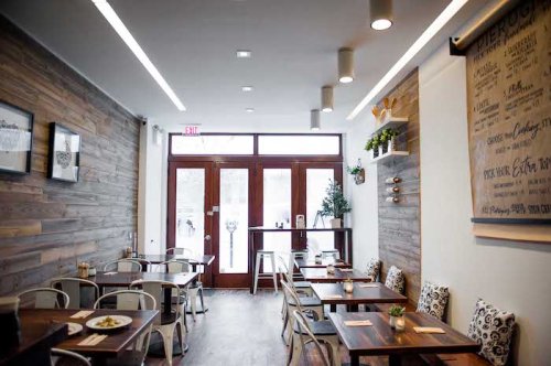 Bright, modern restaurant interior with wooden walls, tables, and plants, featuring large windows and a welcoming atmosphere.