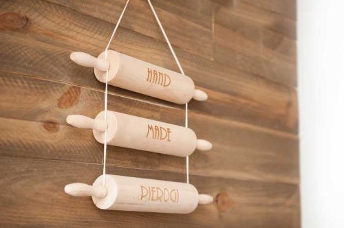 Three wooden rolling pins hanging on a wooden wall, engraved with the words "HAND," "MADE," and "PIEROGI."