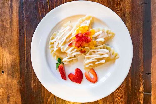 A plate of dumplings drizzled with sauce, topped with diced fruit and garnished with strawberries shaped like a heart.