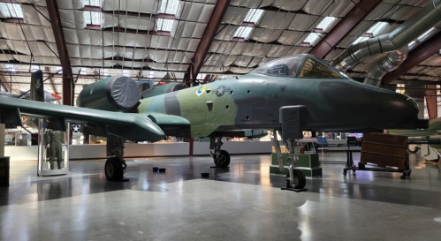 A military aircraft displayed in a museum, featuring a green camouflage pattern and positioned on a concrete floor.