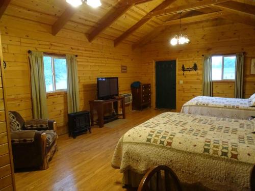 Cozy wooden cabin interior with two beds, a TV, and a seating area, featuring warm lighting and rustic decor.