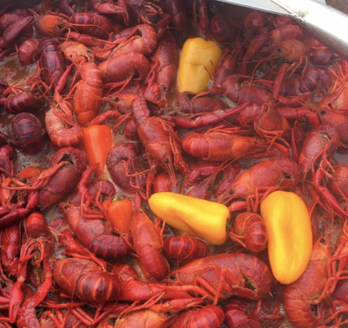 A close-up of cooked crawfish mixed with yellow and orange bell peppers in a pot.