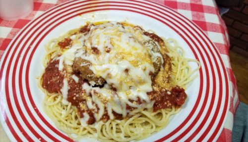 A plate of spaghetti topped with marinara sauce, melted cheese, and a breaded meat patty, served on a red-striped plate.