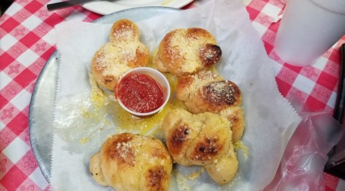 A plate of golden-brown garlic knots with a side of marinara sauce on a checkered tablecloth.