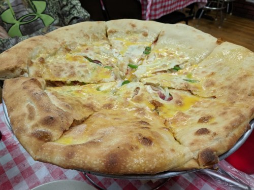 A large, freshly baked pizza with melted cheese, green peppers, and slices cut into wedges on a round tray.