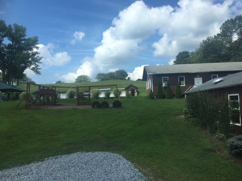 A grassy area with a playground, a building, and trees under a blue sky with fluffy clouds.