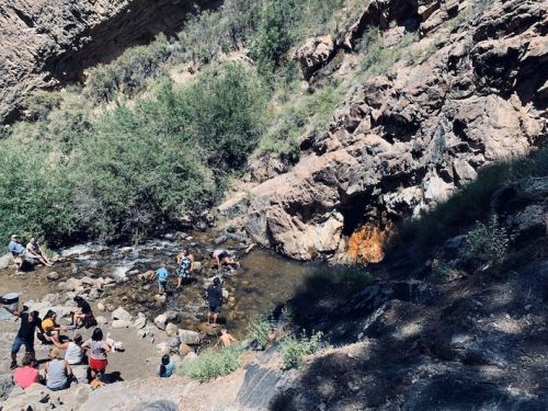 People gather by a rocky stream surrounded by greenery, enjoying the natural landscape and water activities.