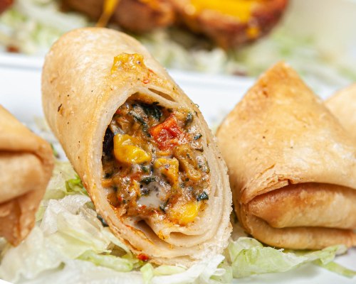 Close-up of crispy rolled tortillas filled with colorful vegetables and cheese, served on a bed of lettuce.