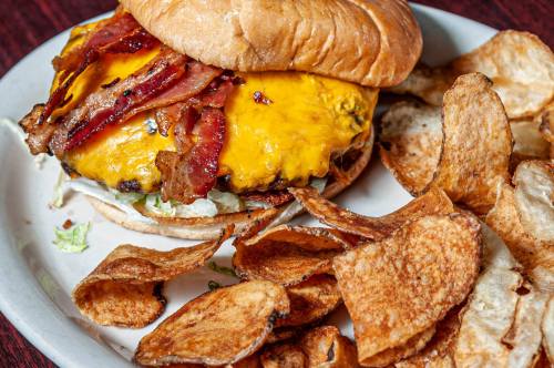 A juicy cheeseburger topped with bacon on a bun, served with crispy potato chips on the side.