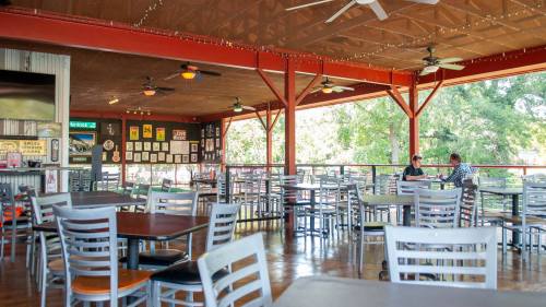 A spacious restaurant interior with empty tables and two people dining at a corner table under ceiling fans.