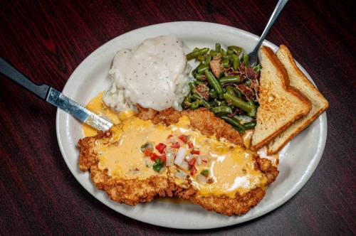 A plate featuring fried chicken topped with cheese, mashed potatoes with gravy, green beans, and toasted bread.
