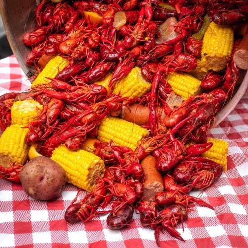 A vibrant spread of red crawfish, corn on the cob, potatoes, and sausage on a checkered tablecloth.