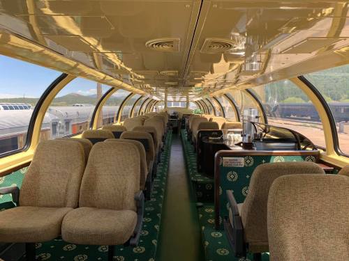 Interior of a vintage train car featuring plush seating and large windows, with a green carpet and a clean, spacious layout.