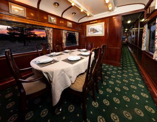 Elegant dining area in a vintage train car, featuring a set table and large windows with a sunset view.