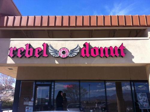 Sign for "rebel donut" with wings, displayed on a storefront under a clear blue sky.
