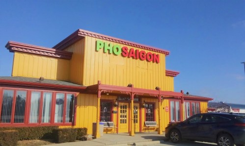 Bright yellow restaurant exterior with "PHO SAIGON" sign, featuring red and green letters against a clear blue sky.