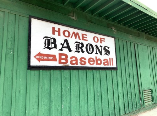 Sign reading "Home of Barons Baseball" on a green wooden wall, with an arrow pointing to "Office Upstairs."