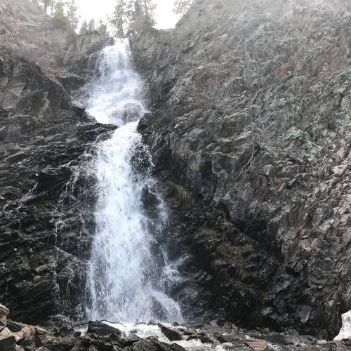 A cascading waterfall flows down rocky cliffs, surrounded by sparse trees and rugged terrain.