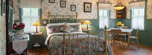 Cozy bedroom with floral wallpaper, a brass bed, and a small dining table, illuminated by warm lamps.