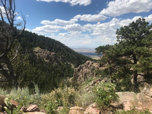 A scenic view of a mountainous landscape with lush greenery, rocky cliffs, and a blue sky dotted with clouds.