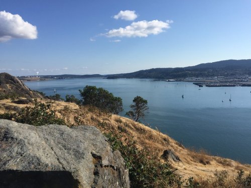 A serene view of a river surrounded by hills, with boats in the water and a clear blue sky above.