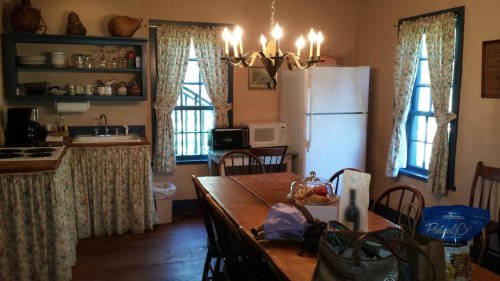 Cozy kitchen with a wooden table, floral curtains, a chandelier, and appliances like a fridge and microwave.