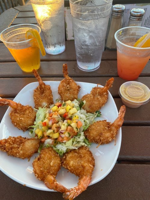 A plate of crispy fried shrimp arranged around a fresh salad with mango salsa, accompanied by drinks.