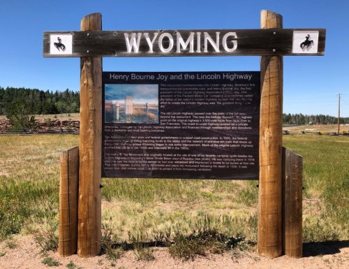 Signpost in Wyoming detailing Henry Bourne Joy and the Lincoln Highway, with a scenic background of grass and trees.