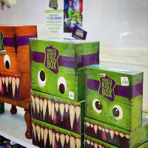 Colorful boxes with monster faces and sharp teeth, labeled "Monster Kidz Box," stacked in a playful display.