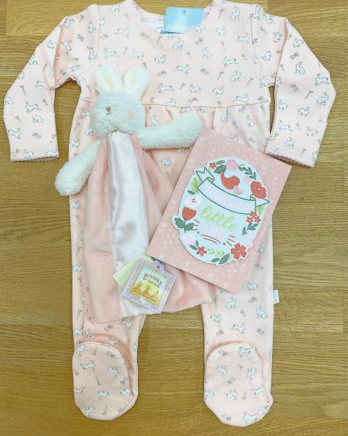 A pink baby onesie with bunny prints, a plush bunny toy, and a welcome card on a wooden surface.