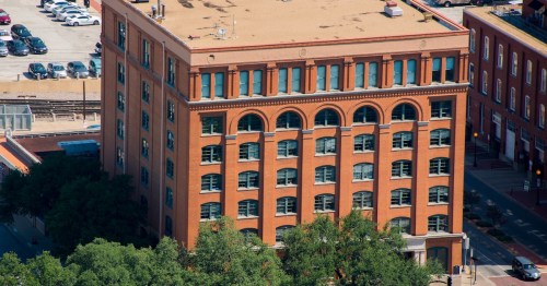 Aerial view of the red brick Sixth Floor Museum in Dallas, TX, formerly the Texas School Book Depository.