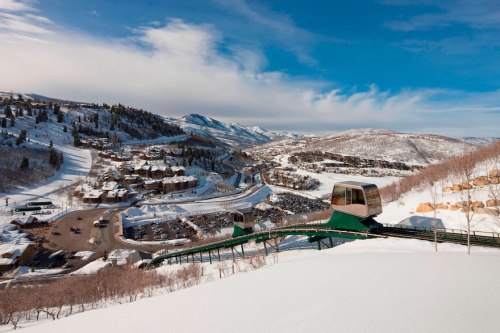 A scenic winter landscape featuring a ski lift, snow-covered mountains, and a small town below.