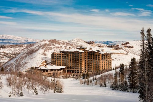 A large wooden hotel nestled in a snowy mountain landscape under a clear blue sky.