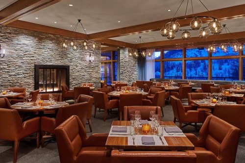 Cozy restaurant interior with wooden accents, stone walls, and warm lighting, featuring tables set for dining.