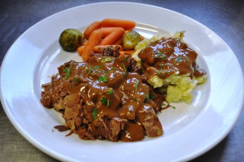A plate of sliced roast beef with gravy, mashed potatoes, carrots, and Brussels sprouts.
