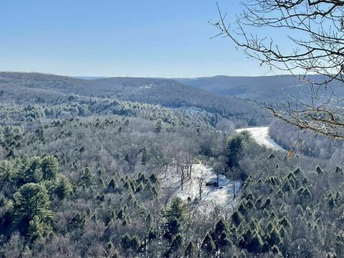 A panoramic view of a snowy landscape with rolling hills, trees, and a winding river under a clear blue sky.
