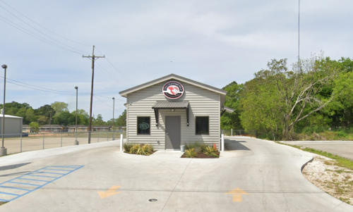 A small, modern building with a circular sign, surrounded by greenery and a paved driveway.