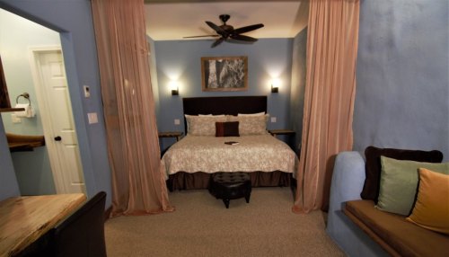 Cozy bedroom with a king-sized bed, soft lighting, and a seating area, featuring blue walls and elegant decor.