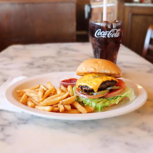 A cheeseburger with lettuce, tomato, and fries on a plate, accompanied by a glass of Coca-Cola.