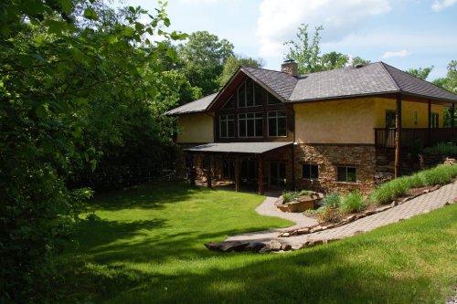 A modern two-story house with a stone facade, surrounded by greenery and a well-maintained lawn.