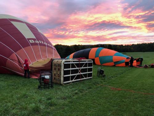 Two hot air balloons being inflated on a grassy field at sunrise, with vibrant colors against a cloudy sky.