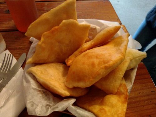 A basket of golden, crispy fried pastries stacked on a wooden table.