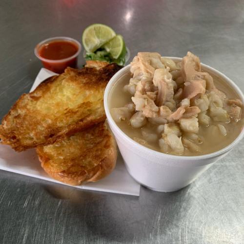A cup of hearty soup with chicken and rice, served with toasted bread and lime wedges on the side.