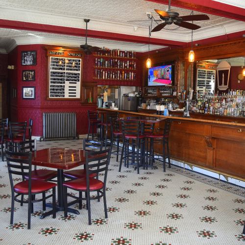 A cozy bar interior with wooden furniture, a well-stocked bar, and decorative tile flooring.