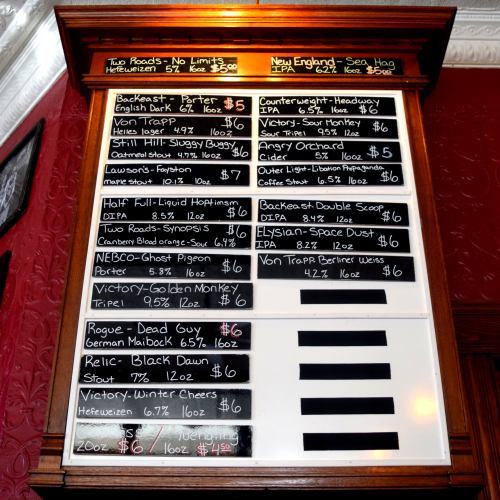 A chalkboard menu displaying various beers and prices in a pub setting.
