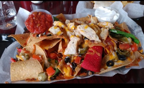 A large plate of nachos topped with chicken, cheese, jalapeños, olives, and served with salsa and sour cream.