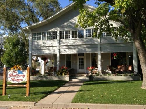 A charming two-story house with a sign reading "The Balcony House," surrounded by greenery and colorful flowers.