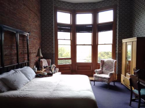 Cozy bedroom with a brick wall, large windows, floral armchairs, and a wooden wardrobe, creating a warm atmosphere.