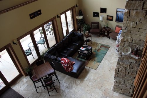 A spacious living room with a black sofa, coffee table, and dining area, featuring large windows and stone accents.