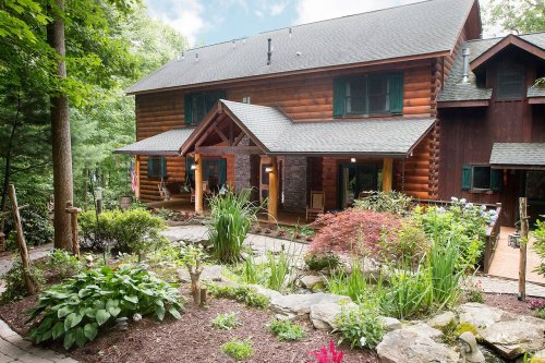 A charming log cabin surrounded by lush greenery and colorful flowers, featuring a welcoming front porch.